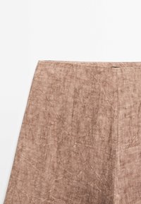 Gros plan d’une jupe texturée marron montrant la taille et des détails subtils de couture verticale sur fond blanc.