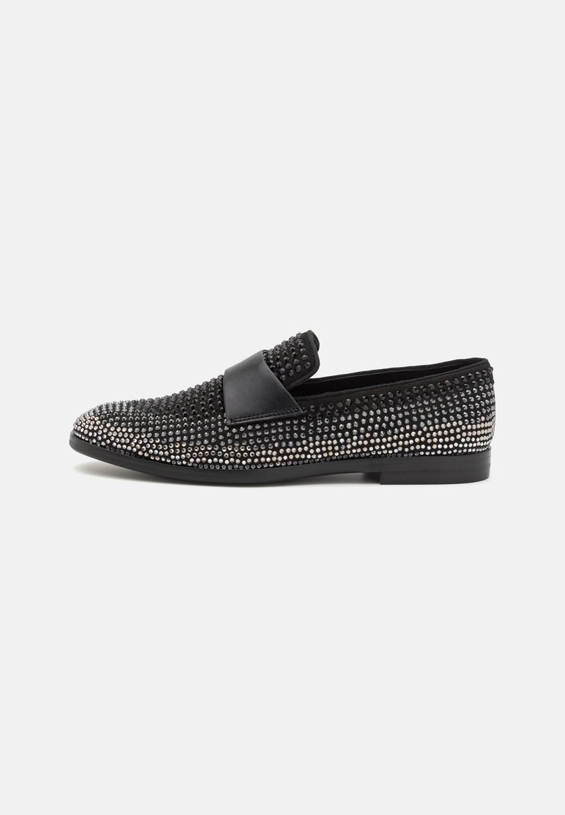 Chaussure noire à enfiler avec des clous argentés recouvrant la surface et une sangle noire lisse sur le dessus, vue de profil.