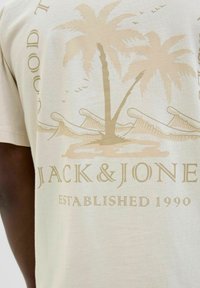 Bež majica od pamuka s grafikom palme u svijetlosmeđoj boji, s natpisom "JACK & JONES" i datumom osnivanja otisnutim ispod.