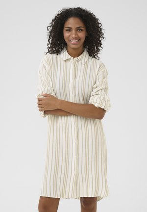 Knopfhemdkleid in Creme mit beigen vertikalen Streifen. Der Stoff wirkt leicht, mit aufgerollten Ärmeln und einem lockeren Schnitt.