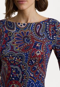 Top con motivo paisley multicolore in blu, rosso e oro. Presenta un ampio scollo e maniche lunghe con dettagli floreali intricati.