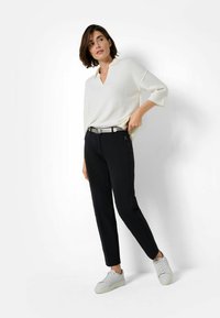Pull léger en crème avec décolleté en V et manches trois-quarts, associé à un pantalon noir ajusté et des baskets blanches. Ceinture en argent en accent.