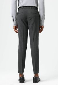 Grijze, op maat gemaakte broek met een smalle pasvorm, decoratieve achterzakken en een gladde textuur. Gecombineerd met zwart schoeisel.