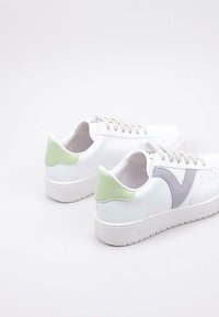 Baskets blanches avec une surface texturée, accents gris et languette de talon vert pastel. Six œillets avec des lacets gris clair ; semelle en caoutchouc.