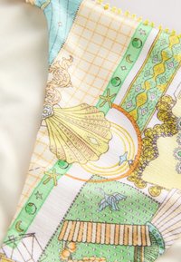 Lähikuva kankaasta, jossa on simpukan, meritähtien, kuun sekä monimutkaisten geometristen ja kukkaisten kuvioiden kuvioita pastellinvihreissä, keltaisissa ja oransseissa sävyissä.