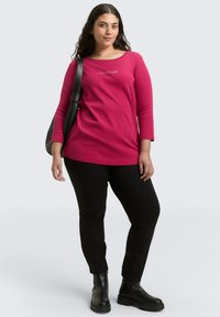 Fuchsias farbener Langarm-Top mit rundem Ausschnitt und dem "TOM TAILOR"-Logo, kombiniert mit schwarzen, enganliegenden Hosen und klobigen schwarzen Stiefeletten.