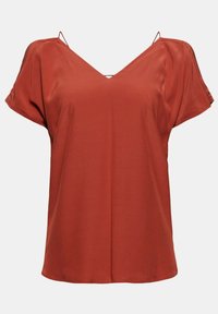 Blusa de color óxido con escote en V y mangas cortas. Textura suave, corte relajado y pequeños recortes diagonales en los hombros.