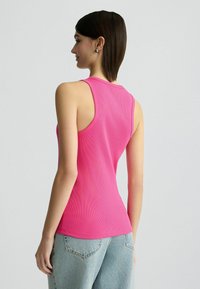 Helles pinkes geripptes Tanktop mit einem runden Ausschnitt und weiten Armausschnitten, kombiniert mit hellblauen hoch geschnittenen Jeans.