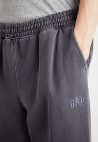 Mørkegrå joggebukser med elastisk liv og sidelommer. Har brodert "GAP"-logo i lyseblått på venstre lår.