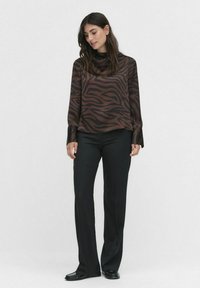Blouse marron à rayures zébrées avec des manches longues, associée à un pantalon noir et des chaussures plates. Tissu doux avec une coupe décontractée et un léger éclat.