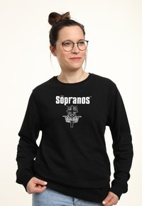 Felpa nera con logo "I Soprano" e grafica di una croce e una corona in bianco. Tessuto morbido, polsini e orlo a costine, vestibilità casual.