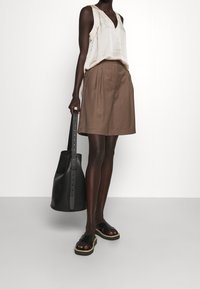 Blusa senza maniche beige, gonna plissettata marrone, borsa in pelle nera con tracolla e sandali neri con suole intrecciate. Design semplice e pulito.