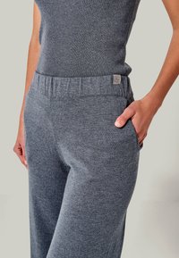 Gray knit pants with a soft texture, featuring an elastic waistband and a side pocket. A small logo tag is visible on the waistband.