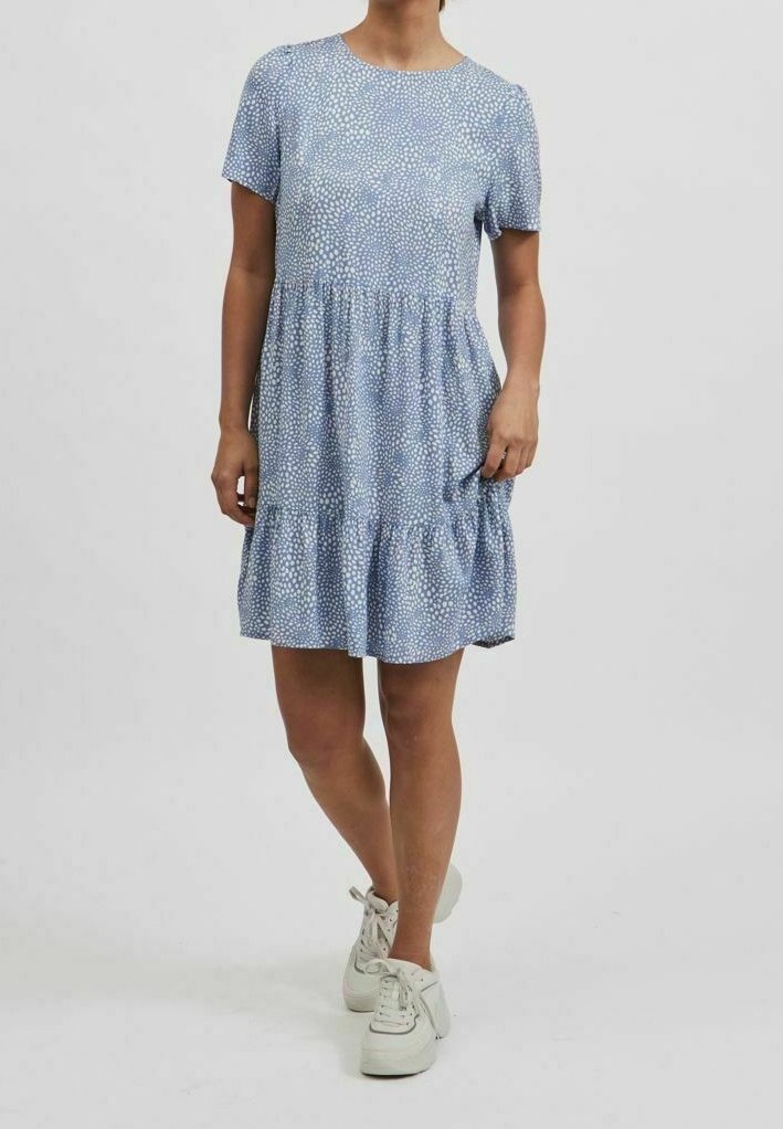 Blå klänning med kort ärm och en lagd kjol, prydd med ett strukturerat mönster av små vita prickar. Bärs med vita sneakers.