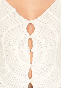 Top bianco lavorato a maglia con scollatura a V profonda, chiusura a bottoni circolari e texture a costine con dettagli a traforo intorno al seno.