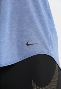Vaaleansininen urheilu paita, joka on valmistettu pehmeästä kankaasta, jossa on musta Nike-logon swoosh helman kohdalla, yhdistettynä mustiin legginsseihin, joissa on kultaisia yksityiskohtia.