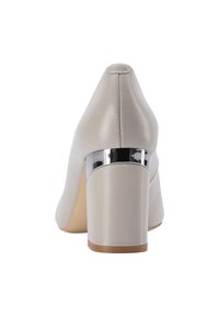 Scarpa con tacco a blocco in pelle beige con un'inserto metallico argento vicino alla parte superiore del tacco, mostrata da dietro su uno sfondo bianco.