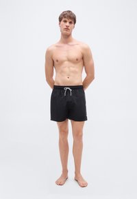 Μαύρο μαγιό βερμούδα με ελαστική μέση και κορδόνι. Διαθέτει λεία, ελαφριά ύφασμα και μινιμαλιστικό σχέδιο. Χωρίς σχέδια ή διακοσμητικά στοιχεία.