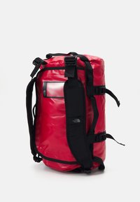 Red backpack with black straps and accents, made of durable material. Features a clear pocket and adjustable buckles. Cylindrical shape.