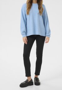 Světle modrý oversize svetr z měkkého pleteného materiálu, spárovaný s černými skinny džíny a robustními černými mokasíny. Jednoduchý výstřih do crew a žebrované manžety.