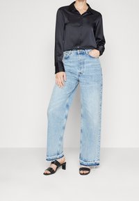 Zwarte satijnen blouse met knoopjes, lichtblauwe wijde jeans met een rafelige zoom en zwarte hoge hakken. Zachte textuur en casual pasvorm.