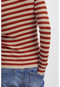 Ribbade tröjan har växelvis röda och beige horisontella ränder. Bärs tillsammans med blå denimjeans som visar detaljer på bakfickan.