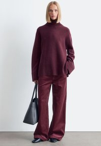 Burgunderfarbener Rollkragenpullover kombiniert mit weiten Cordhosen. Schwarze Ballerinas und eine Ledertasche runden das Outfit ab.