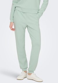 Joggerske hlače v barvi mete, narejene iz mehke tkanine, z elastičnim pasom, stranskimi žepi in zoženimi manšetami. Kombinirane z belimi supergami.