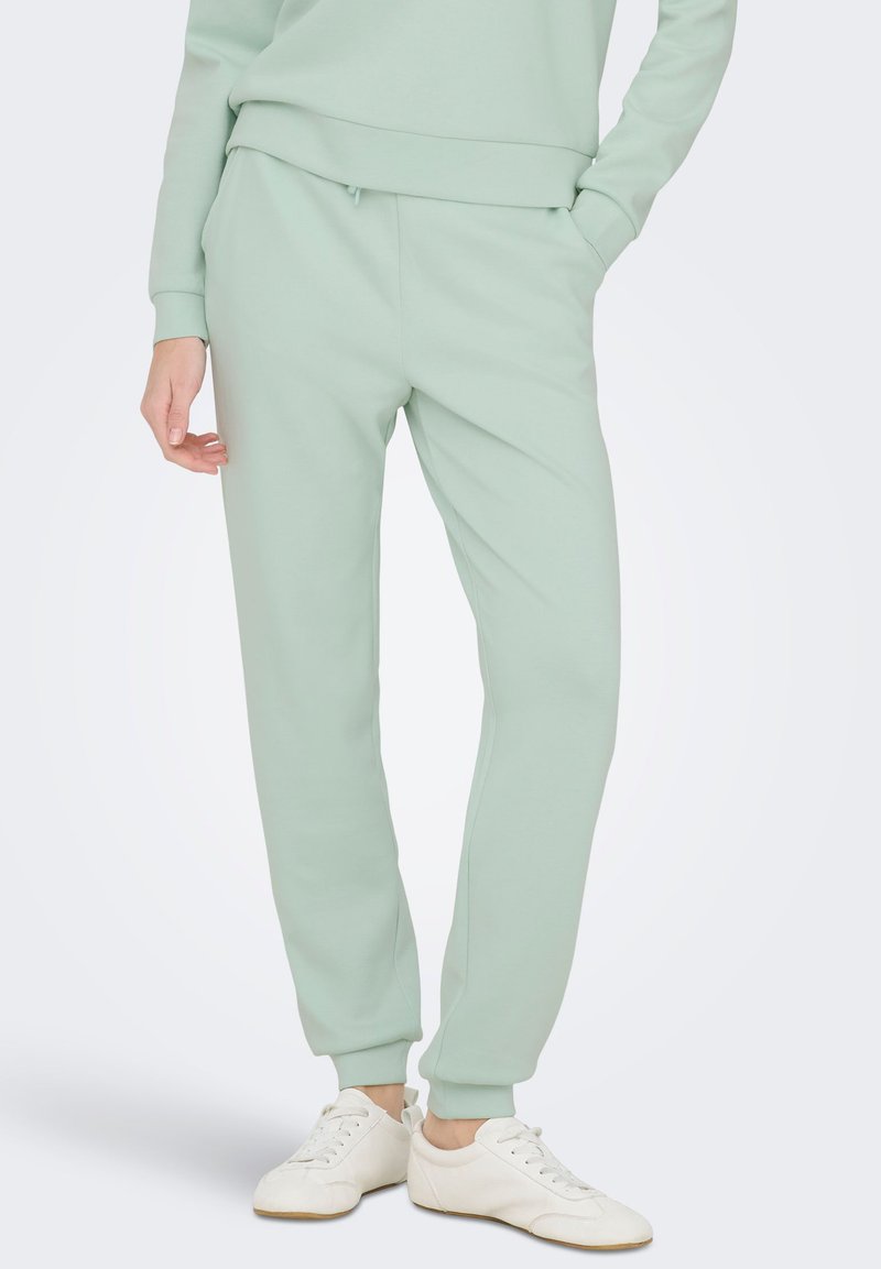 Joggerske hlače v barvi mete, narejene iz mehke tkanine, z elastičnim pasom, stranskimi žepi in zoženimi manšetami. Kombinirane z belimi supergami.