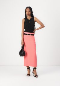 Top negru fără mâneci, cu detalii plisate și guler în formă de cheie; fustă lungă roz cu un brâu negru prevăzut cu accesorii din argint; geantă de mână și tocuri negre.