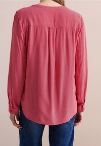 Red and white striped long-sleeve shirt with a round neckline, back pleat detail, and buttoned cuffs, paired with blue denim.