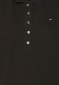 Polo noir en coton texturé, doté d'une patte de boutonnage à trois boutons et d'un petit logo sur la poitrine gauche.