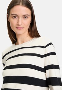 Cremfarbener und schwarzer gestreifter Pullover, weicher Strickstoff, runder Ausschnitt, lockere Passform, horizontale Streifen unterschiedlicher Dicke.