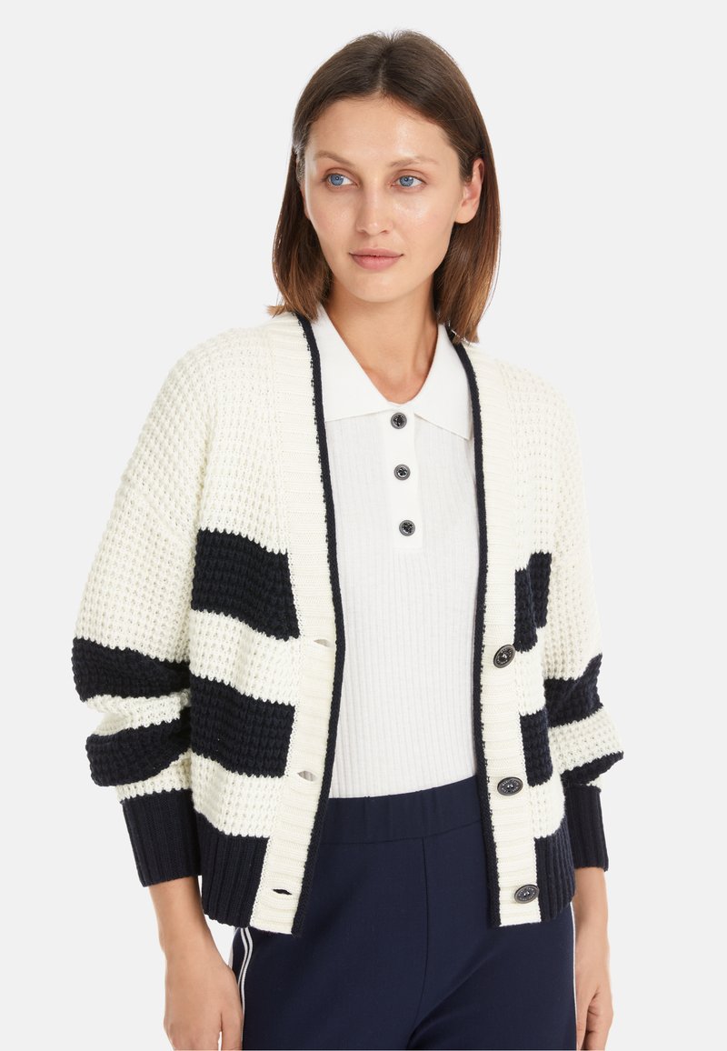 Strickjacke in Creme und Marineblau mit Streifen, ausgestattet mit strukturiertem Stoff, gerippten Bündchen und Knopfverschlüssen, getragen über einem Hemd mit Kragen.