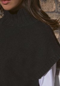 Černý pletený svetr s vysokým žebrovaným límcem a krátkými rukávy, který se vyznačuje jemnou texturou a čistým, minimalistickým designem.