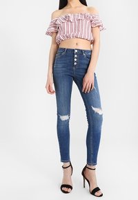Průsvitný pruhovaný top bez ramínek s volánky, kombinovaný s modrými roztrhanými skinny džíny na knoflíky a černými páskovými podpatky.