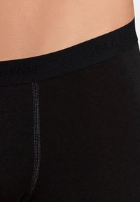 Black underwear featuring a smooth texture, elastic waistband with embossed logo, and contrasting stitching along the seam.