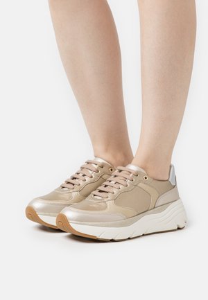 Beżowe buty sportowe z metalicznymi akcentami, górna część z tkaniny i materiałów syntetycznych, okrągły nos, wyściełana podeszwa z teksturowaną, jasną podeszwą.