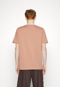 Tričko s krátkým rukávem a kulatým výstřihem v barvě prašné růže, vyrobené z měkké bavlny, s volným střihem a bez viditelných grafik nebo vzorů.