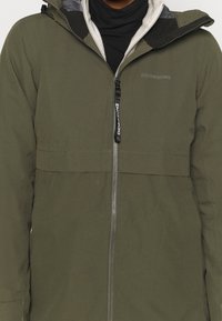 Olijfgroene waterdichte jas met een ritssluiting, fleecgevoerde kraag en verstelbare capuchon; beschikt over een logo op de borst en een praktische vormgeving.