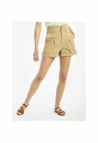 Shorts taille haute kaki avec plis à l'avant, revers et deux poches latérales. Le tissu a une texture lisse et une coupe ajustée.