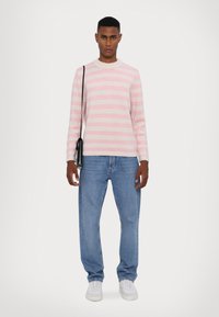 Svetlo roza in bela prugasta pletena jopica, okrogli ovratnik, v kombinaciji z modrimi jeans hlačami in belimi supergami. Majhna črna torbica nošena čez ramo.