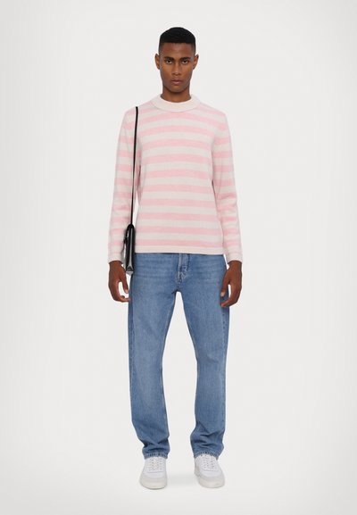 Pull en tricot rayé rose clair et blanc, col rond, associé à un jean en denim bleu et des baskets blanches. Petit sac noir porté en bandoulière.
