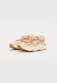 Beige and cream sneakers with orange accents, textured mesh upper, rubber sole, and patterned laces. Rounded toe and padded collar design.