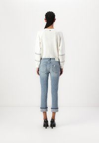 Suéter blanco texturizado con rayas negras, combinado con unos vaqueros de mezclilla azul claro con los puños doblados. Unos zapatos de tacón negros completan el conjunto.