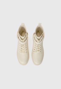 Botas de cuero blancas hasta el tobillo con cordones, acentos de hardware dorado y un zipper lateral. Acabado suave con punta redonda y un ligero tacón.