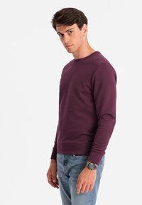 Sweatshirt à col rond violet à manches longues, fabriqué en tissu doux. Dispose de poignets et d'un ourlet côtelés, associé à un jean bleu.