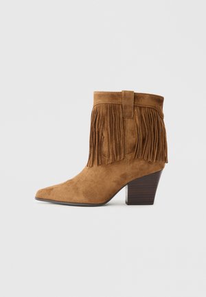 Brown suede ankle boot with a pointed toe, fringe detail at the collar, and a stacked wooden heel. Smooth texture throughout.
