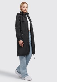 Black parka jacket with a hood, featuring a zip closure and adjustable drawstrings. Made of lightweight fabric, styled with side pockets.