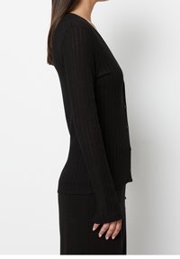 Czarny prążkowany kardigan z długimi rękawami, dekoltem w serek i zapięciem na guziki. Materiał jest miękki, z delikatnym, paskowanym wzorem.